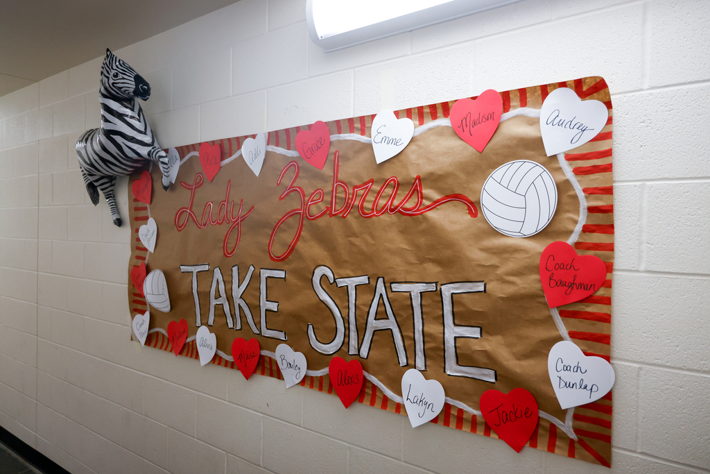 A decorated hallway sign reads “Lady Zebras Take State” with volleyballs and players' names.