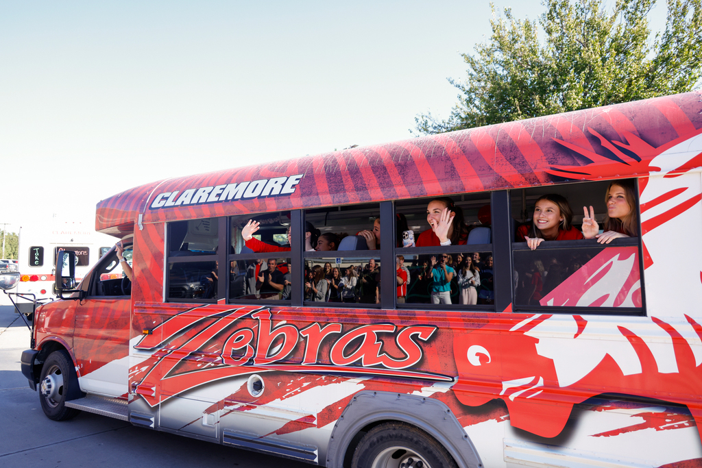 Lady Zebra volleyball players wave from the Zebra bus as students and staff cheer them on.