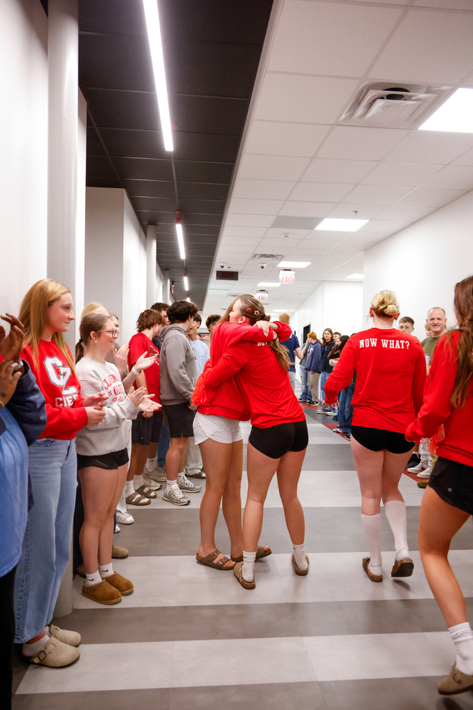 Lady Zebra volleyball players hug as students and staff cheer them on in the hallway.