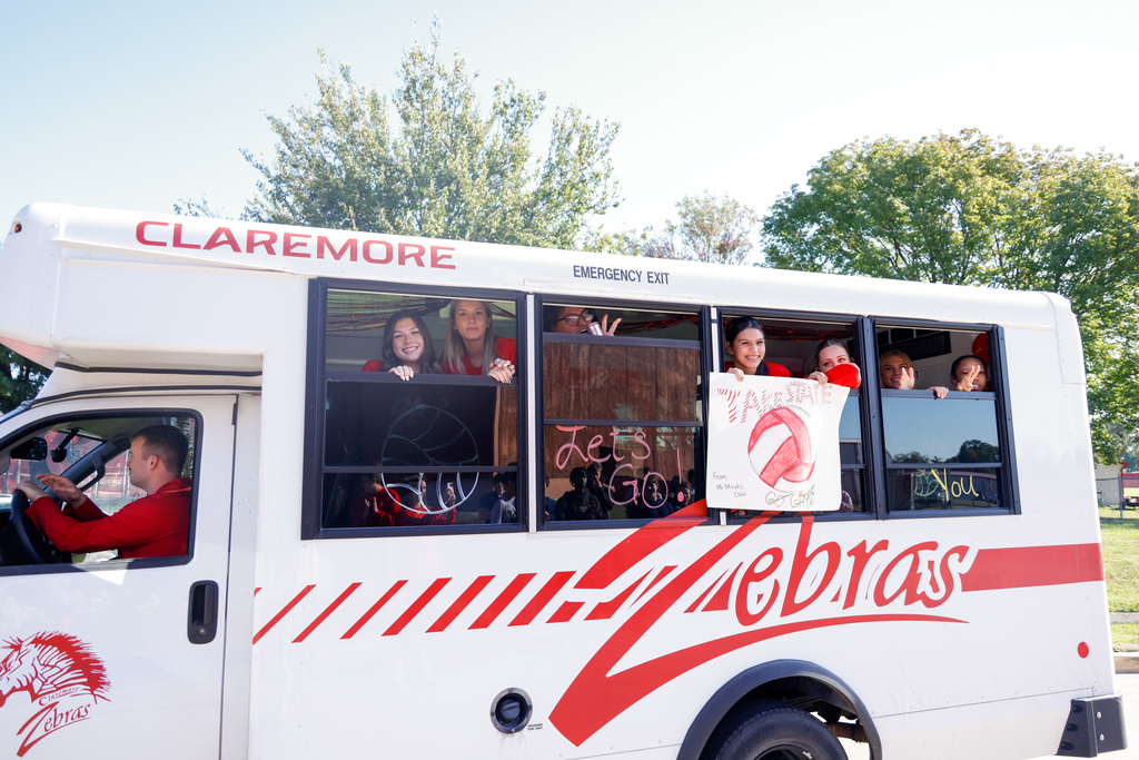 Lady Zebra volleyball players smile and hold signs through the windows of the team bus.
