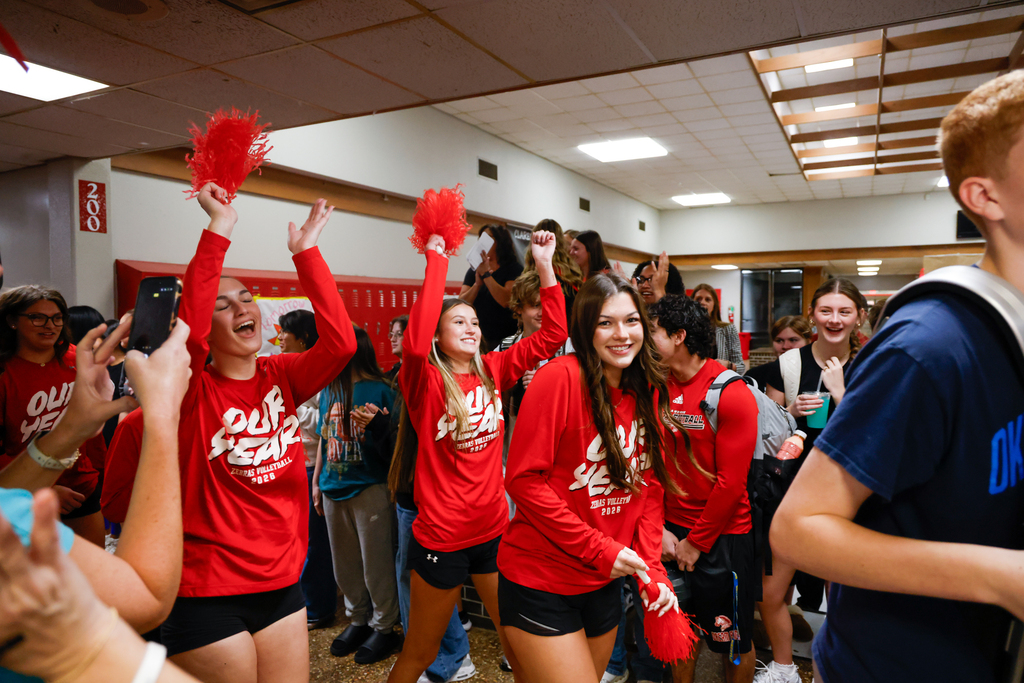Lady Zebra volleyball players wave red pom-poms as students cheer them on.