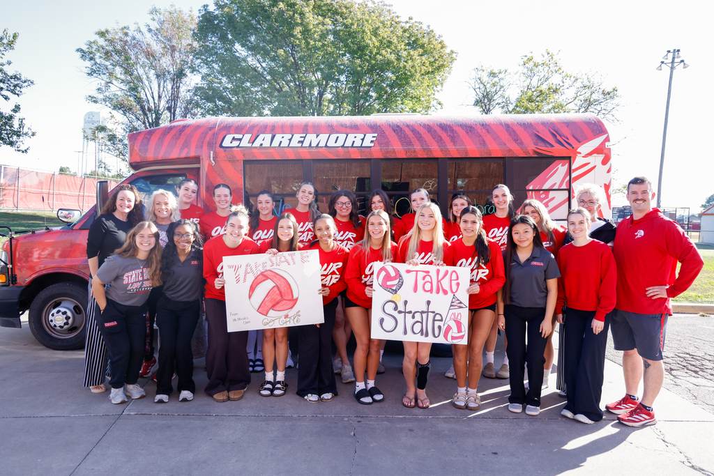 Lady Zebra volleyball players and coaches pose with signs in front of the Claremore Zebra bus.