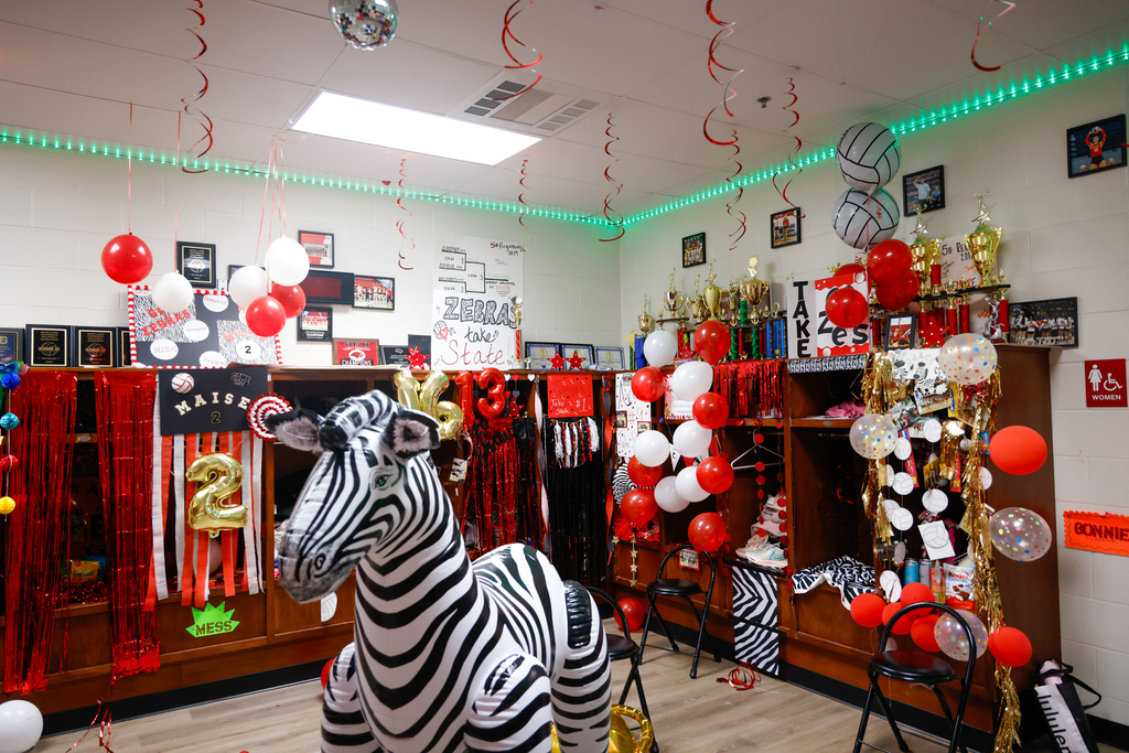 The volleyball locker room is decorated with red and white balloons, streamers, and signs for State.