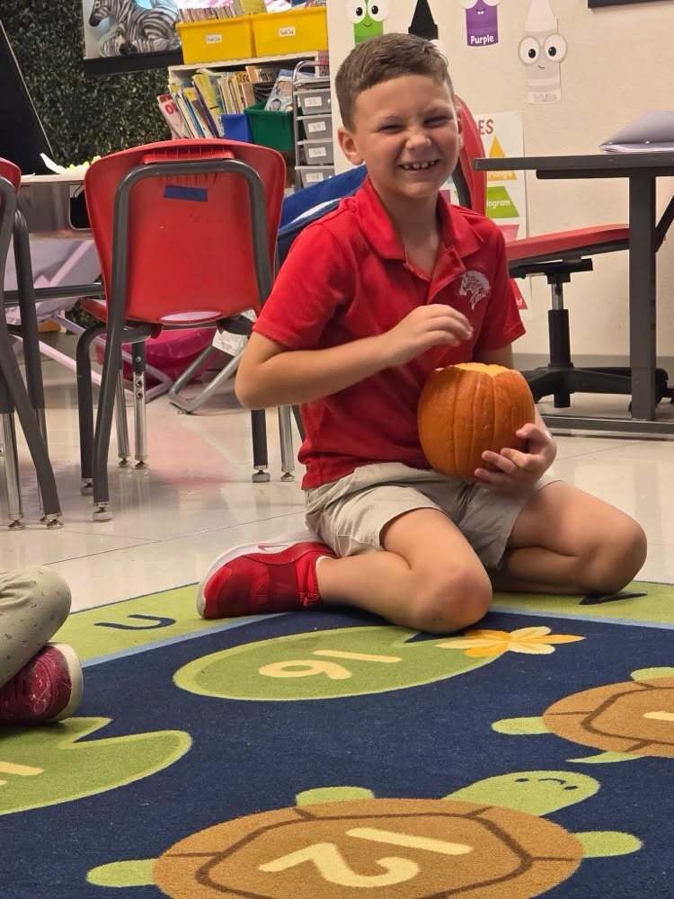 A smiling student in a red shirt holds a small pumpkin during the activity.