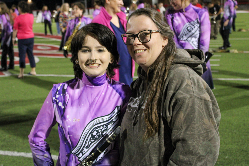 A band student in purple uniform poses with a parent on the field.