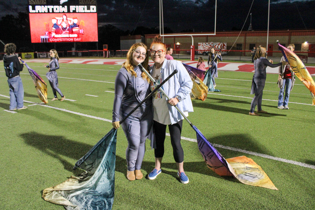 A color guard student and parent pose together holding flags.