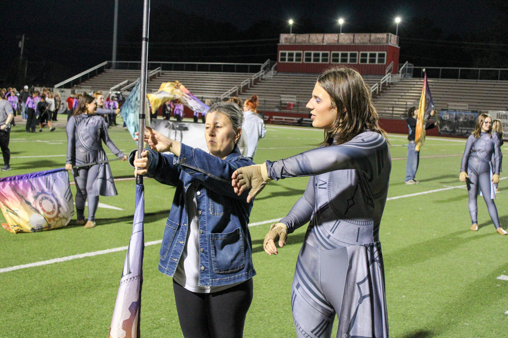 A color guard student teaches a parent how to handle a flag.