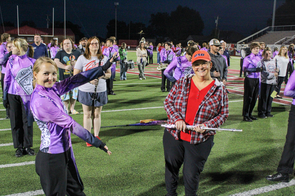 A band student demonstrates marching movements while a parent holds a flute.