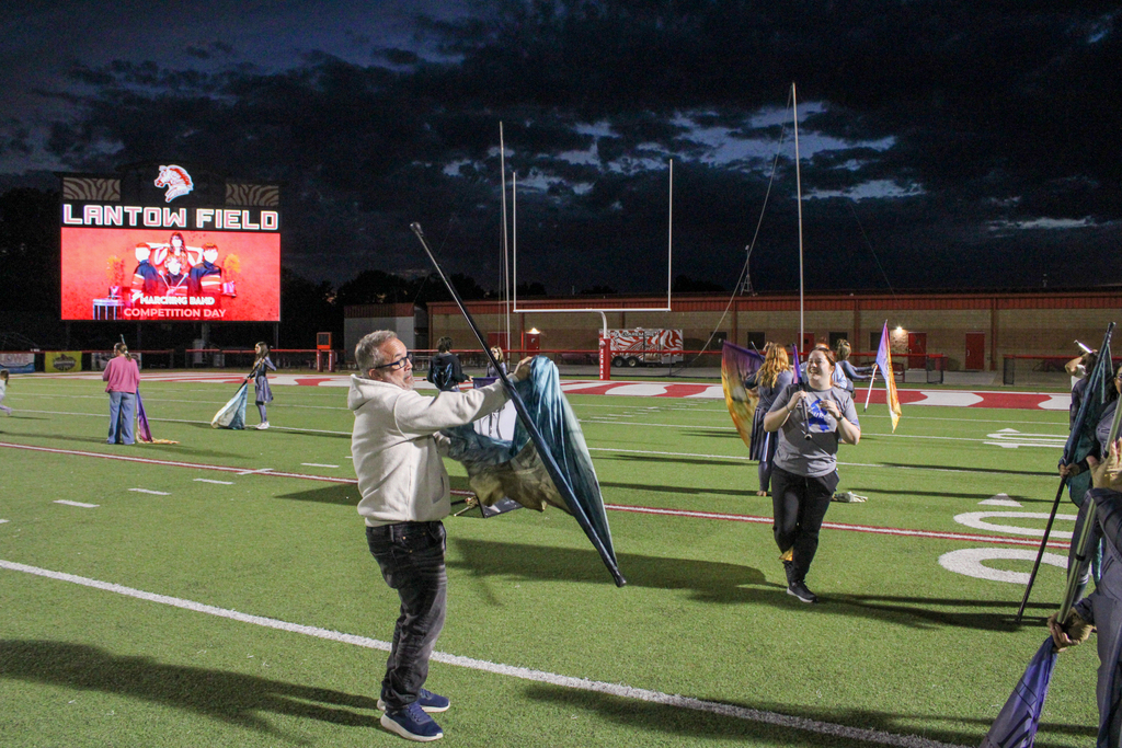 A parent practices spinning a color guard flag on Lantow Field.