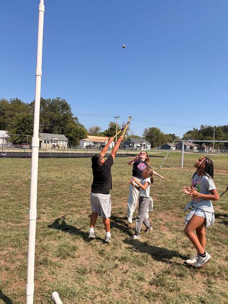 Students reach for a ball with stickball sticks during a Cherokee cultural activity.