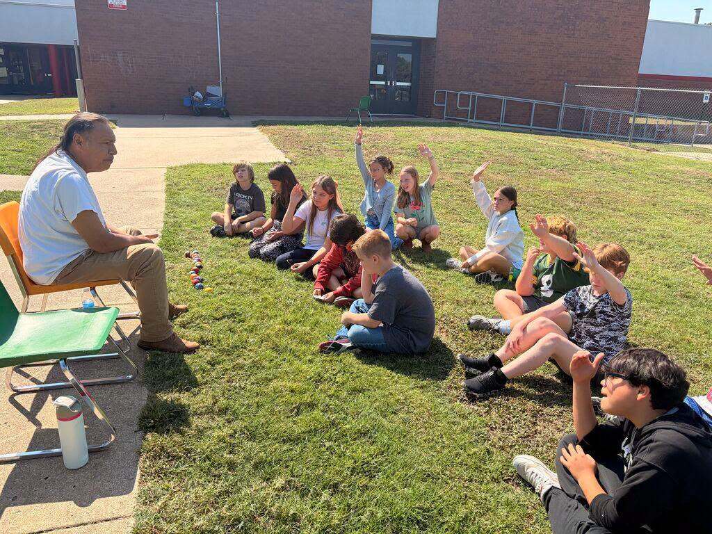 Students listen to a Cherokee cultural presenter and raise their hands.