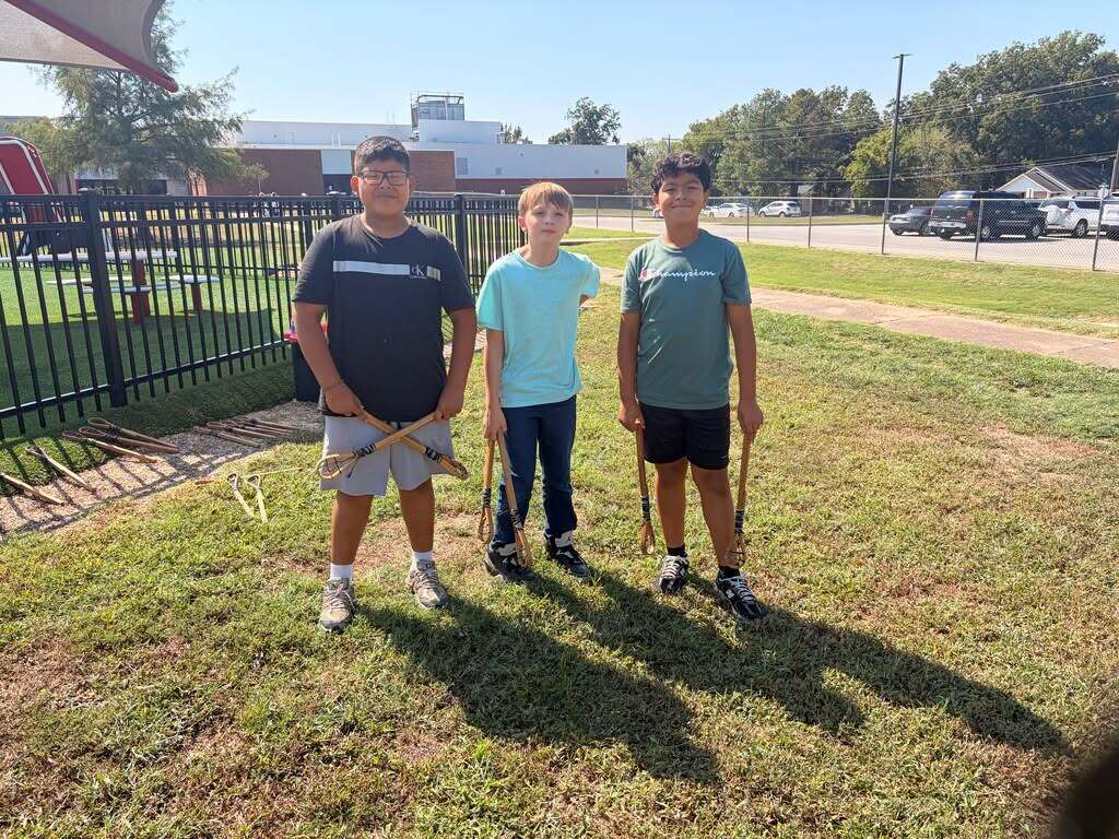 Three students pose with traditional stickball sticks.