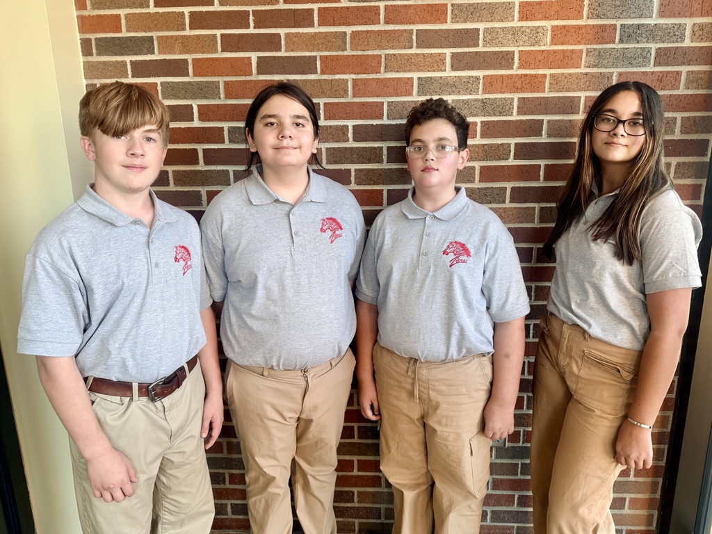 Four Claremore students wearing gray Zebra polos posing together in front of a brick wall.