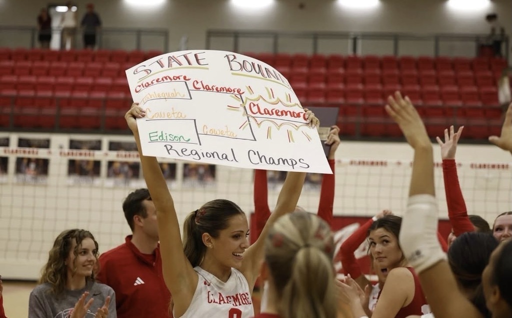 A Claremore volleyball player holds up a State Bound sign while teammates celebrate their Regional Championship.
