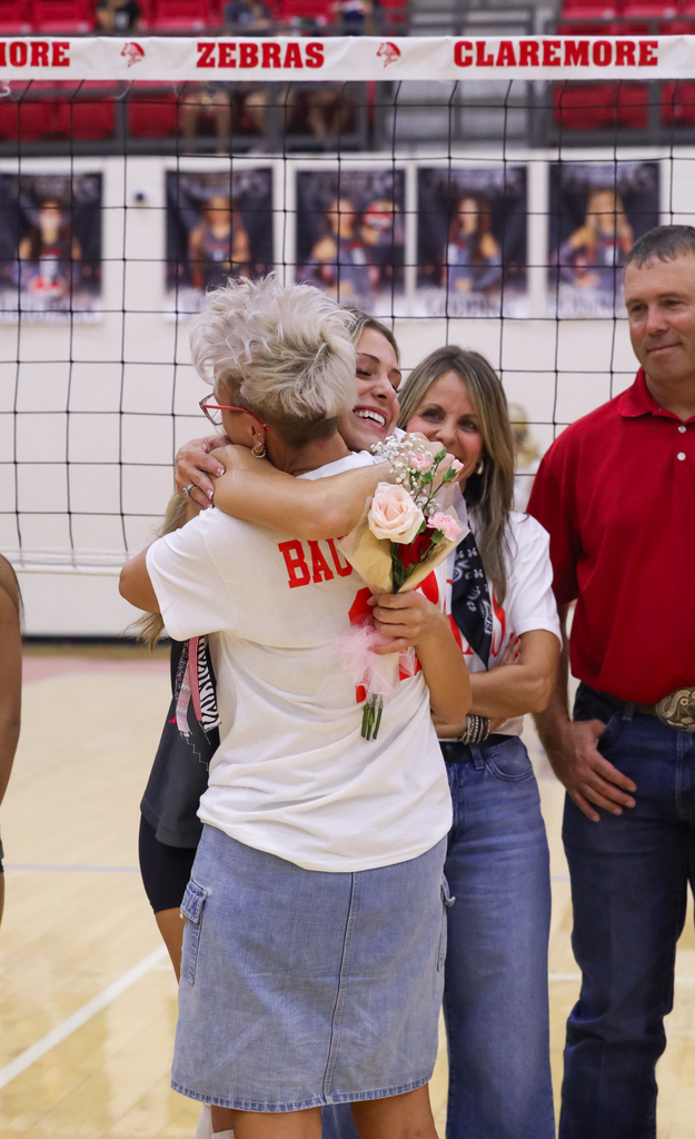 A Claremore volleyball player hugs a loved one while holding flowers during Senior Night.