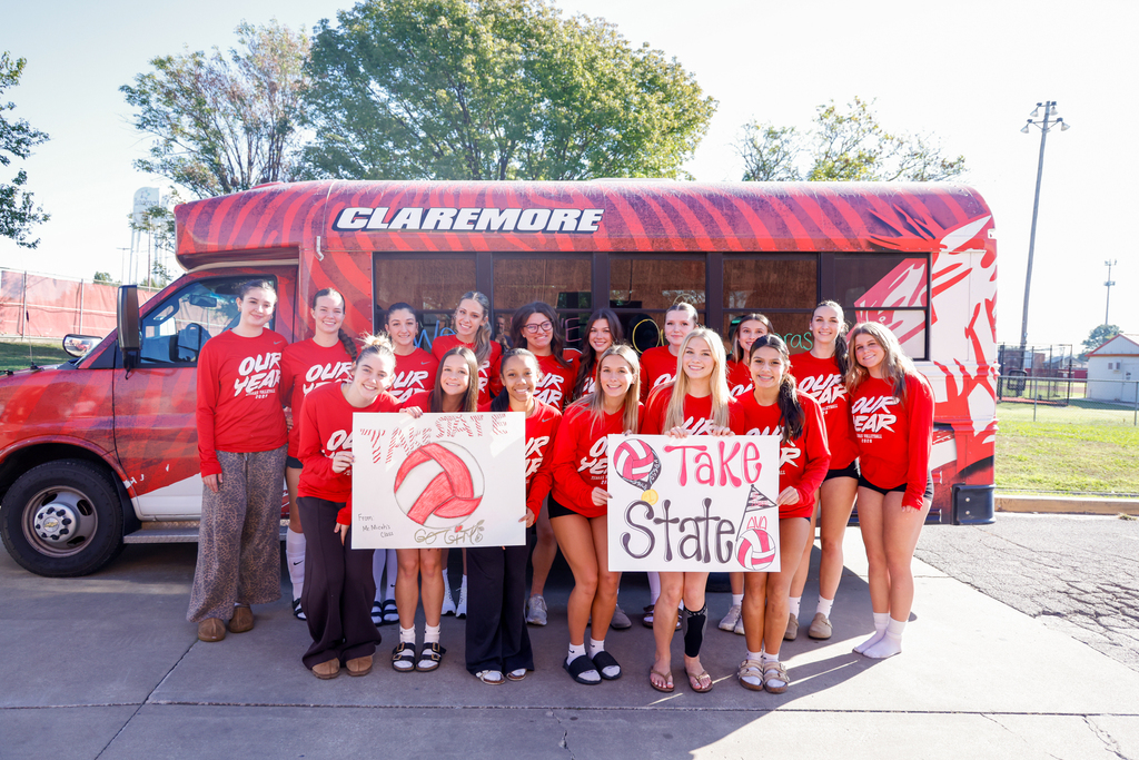 Lady Zebra volleyball players pose with State Bound signs in front of the Zebra bus.