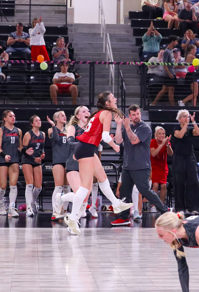 A Lady Zebra volleyball player celebrates with teammates and coaches during a match.