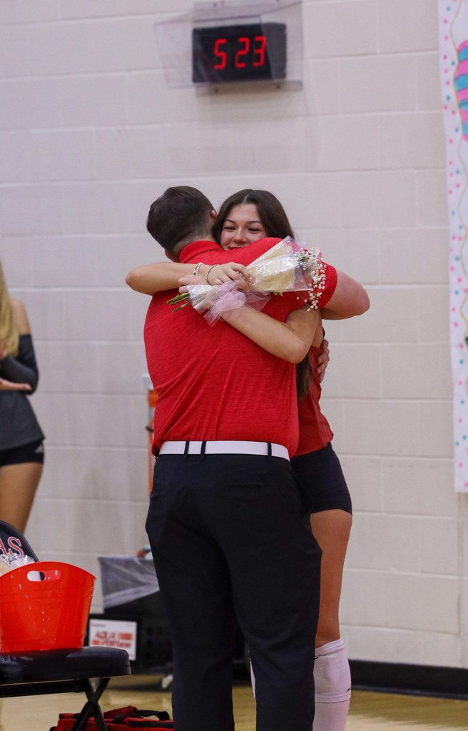 A Lady Zebra volleyball player hugs a family member while holding flowers.
