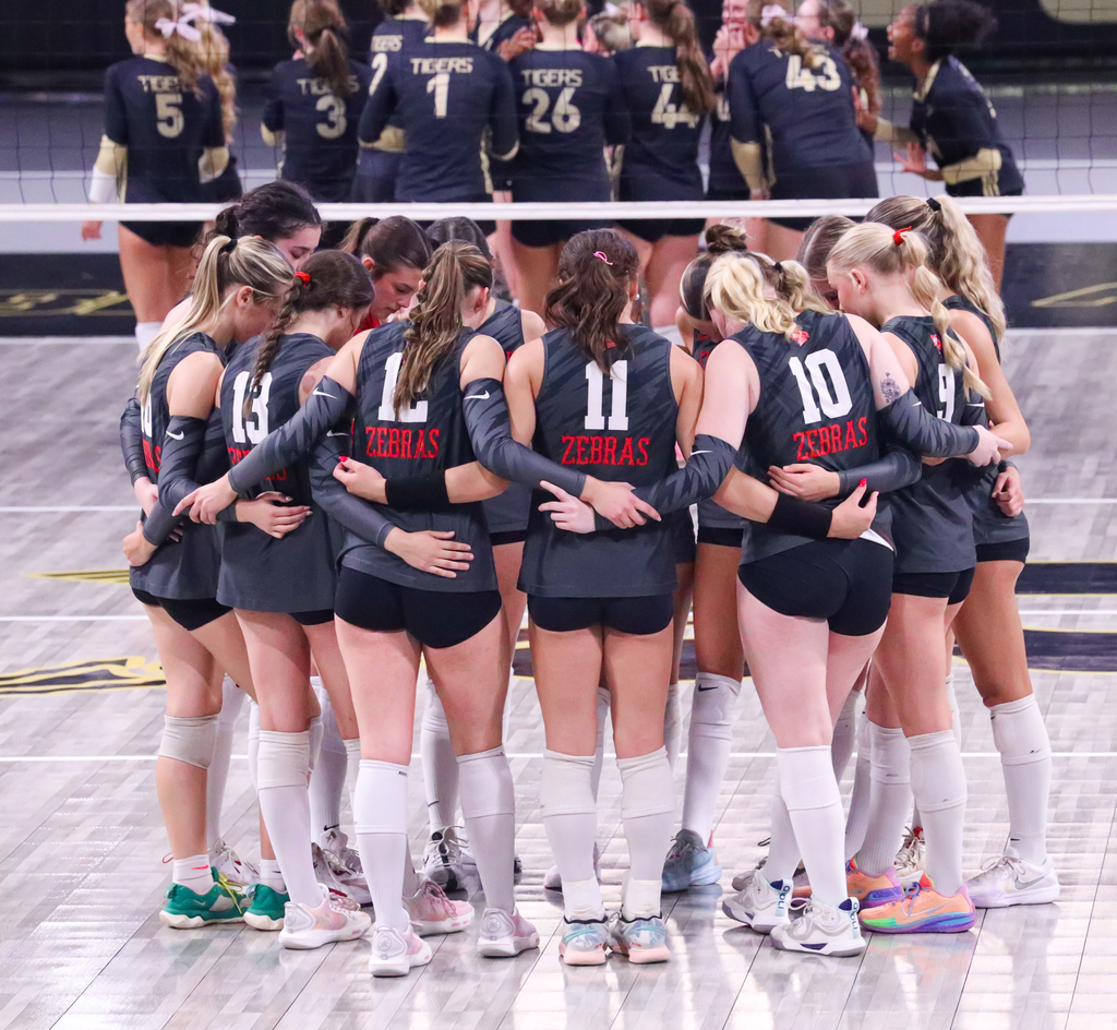 Lady Zebra volleyball players huddle together on the court during the State Tournament.
