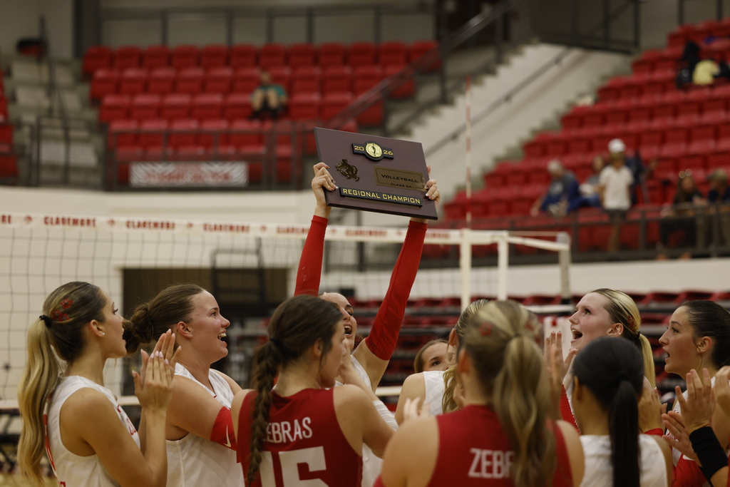 Lady Zebra volleyball players celebrate while holding up their Regional Championship plaque.