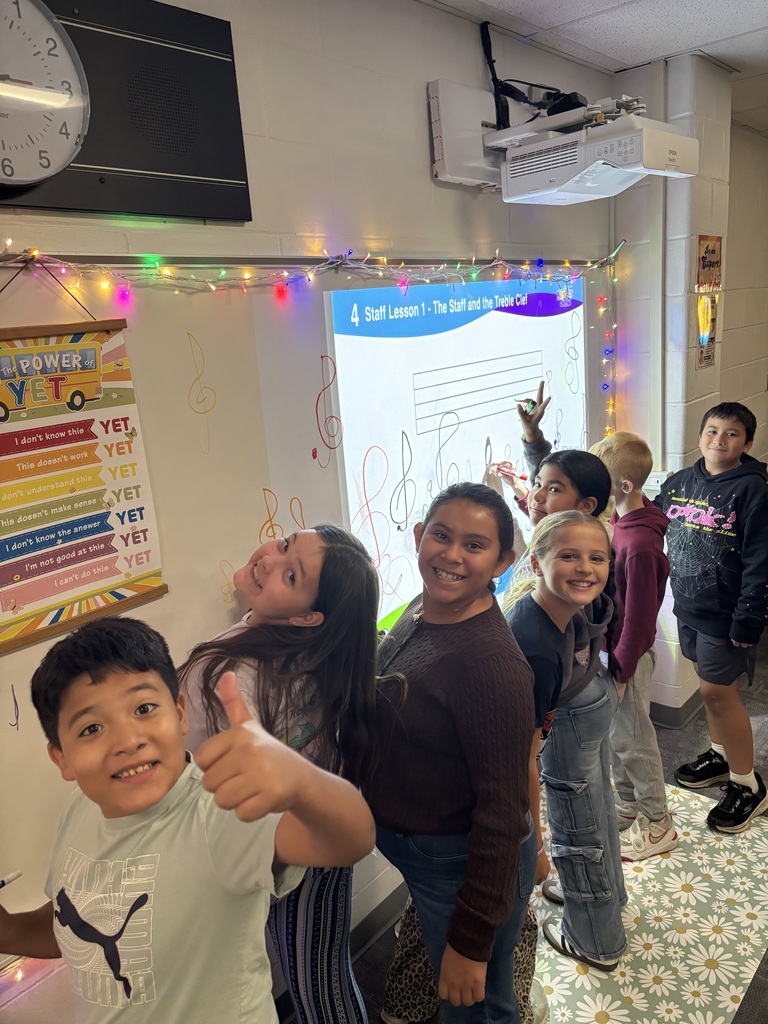 Students practicing drawing treble clefs on the white board in the music classroom.