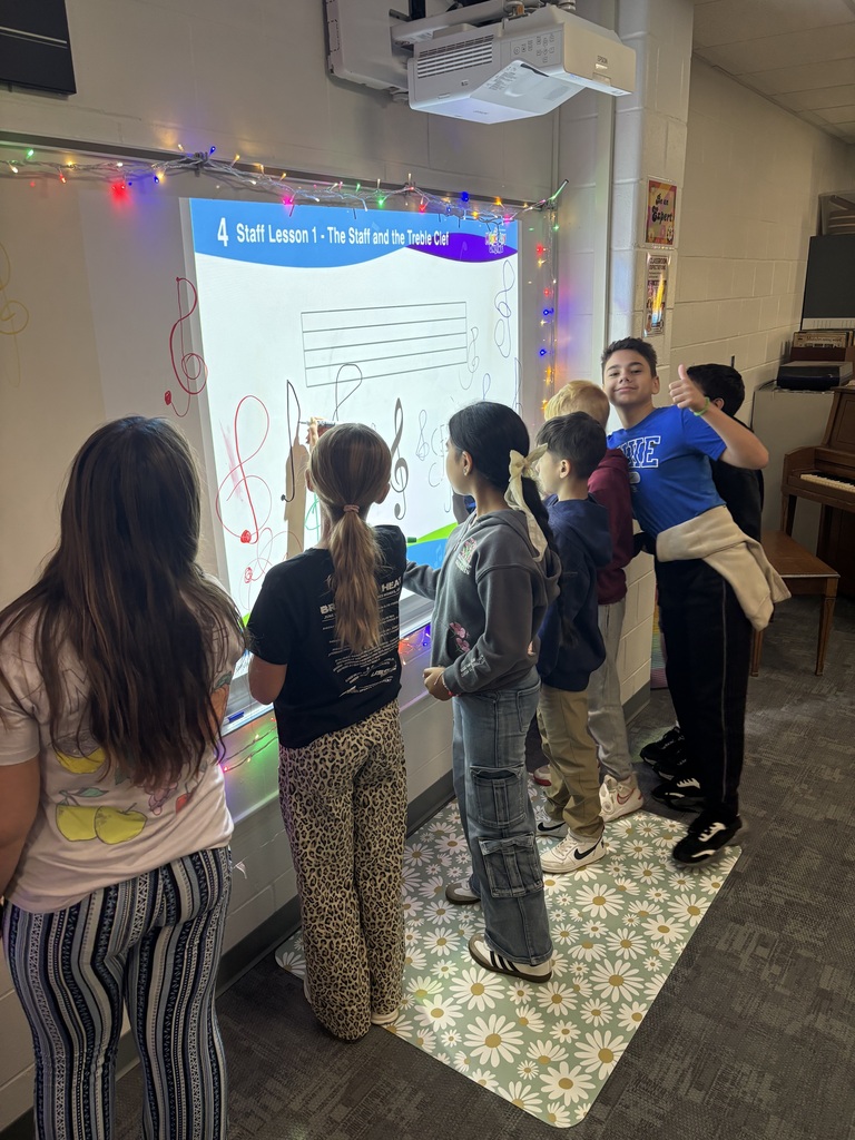 Students practicing drawing treble clefs on the white board in the music classroom.