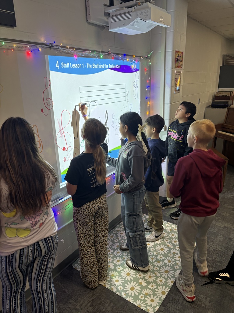Students practicing drawing treble clefs on the white board in the music classroom.