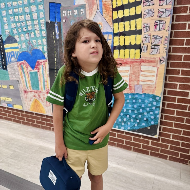 a student holds a lunchbox in front of a mural