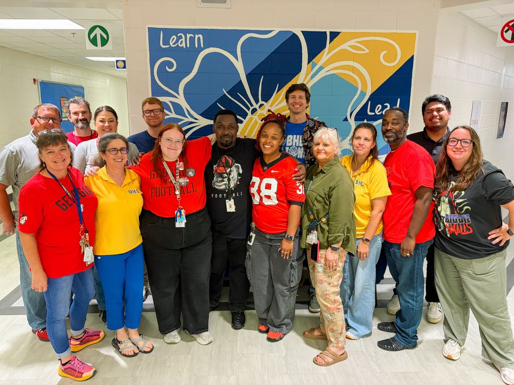An image of the nominees for Teacher of the Year. Teachers are standing in front of the rotunda mural. The mural is blue, white, and yellow and has the word "Lead" written alongside a flower. The teachers appear from left to right in all sorts of brightly colored attire: TOTY: Davina Swaim, Shon Wilson, Todd Elihu, Amanda Irby, Isabel Balsamo, Matthew Rubenstein, Landon Fair, Antony Williams, Daneidra Watkins-Barnett, John Watson, Karen Rhodes, Jessica Shuman, Timothy Mack, Kenny Serrano, and Megan Hardy