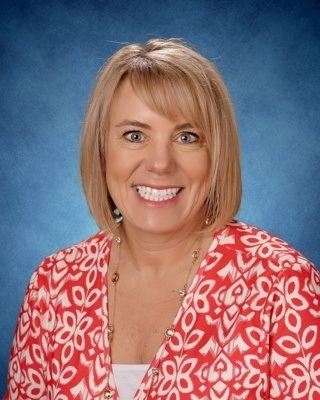 Blonde haired woman in red printed dress with necklace, smiling