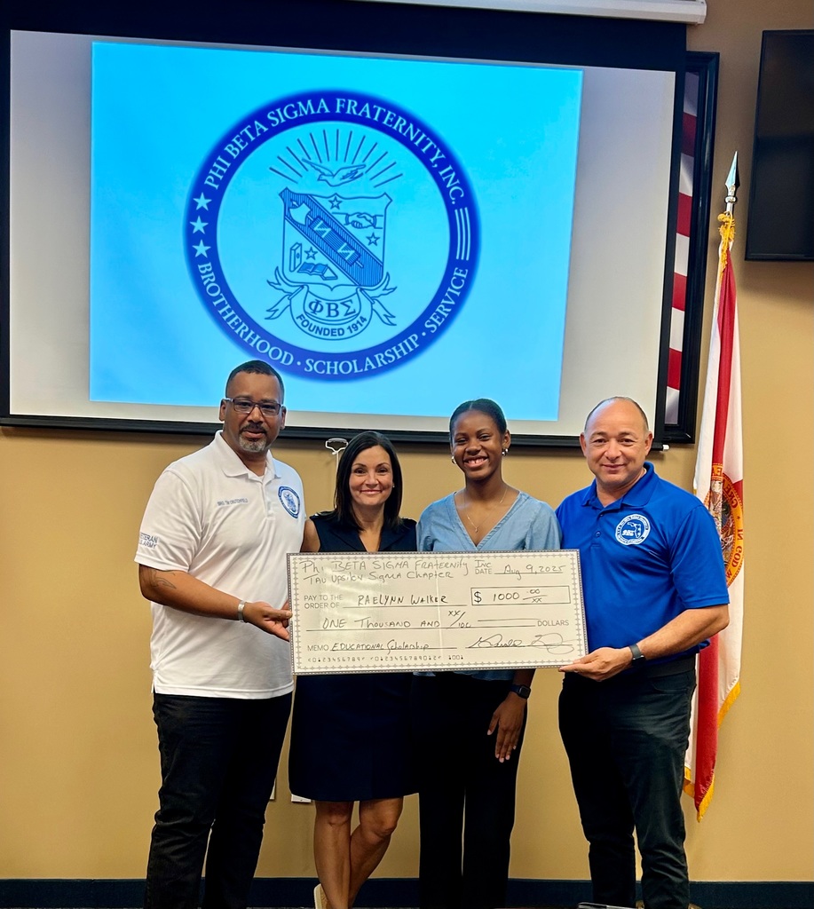 Four people standing together and smiling while holding a large ceremonial check for $1,000 made out to Raelynn Walker from Phi Beta Sigma Fraternity, Inc., Tau Upsilon Sigma Chapter.