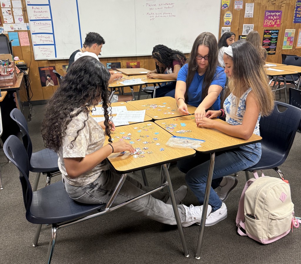 Students sitting at classroom tables working together to assemble puzzles during a team-building activity.