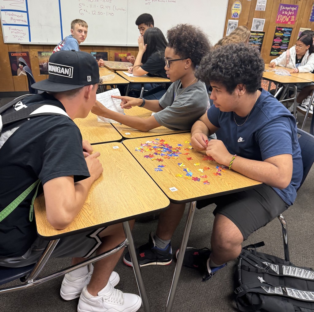 Students sitting at classroom tables working together to assemble puzzles during a team-building activity.