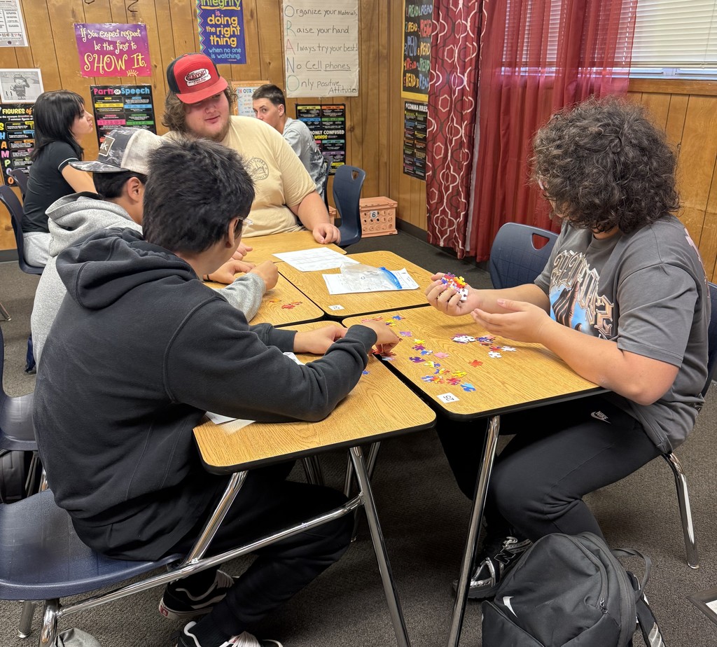 Students sitting at classroom tables working together to assemble puzzles during a team-building activity.