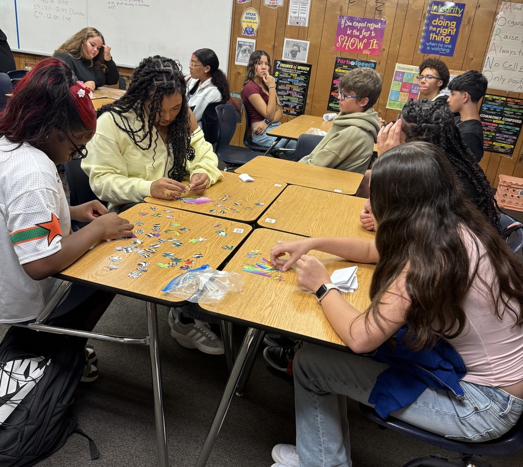 Students sitting at classroom tables working together to assemble puzzles during a team-building activity.