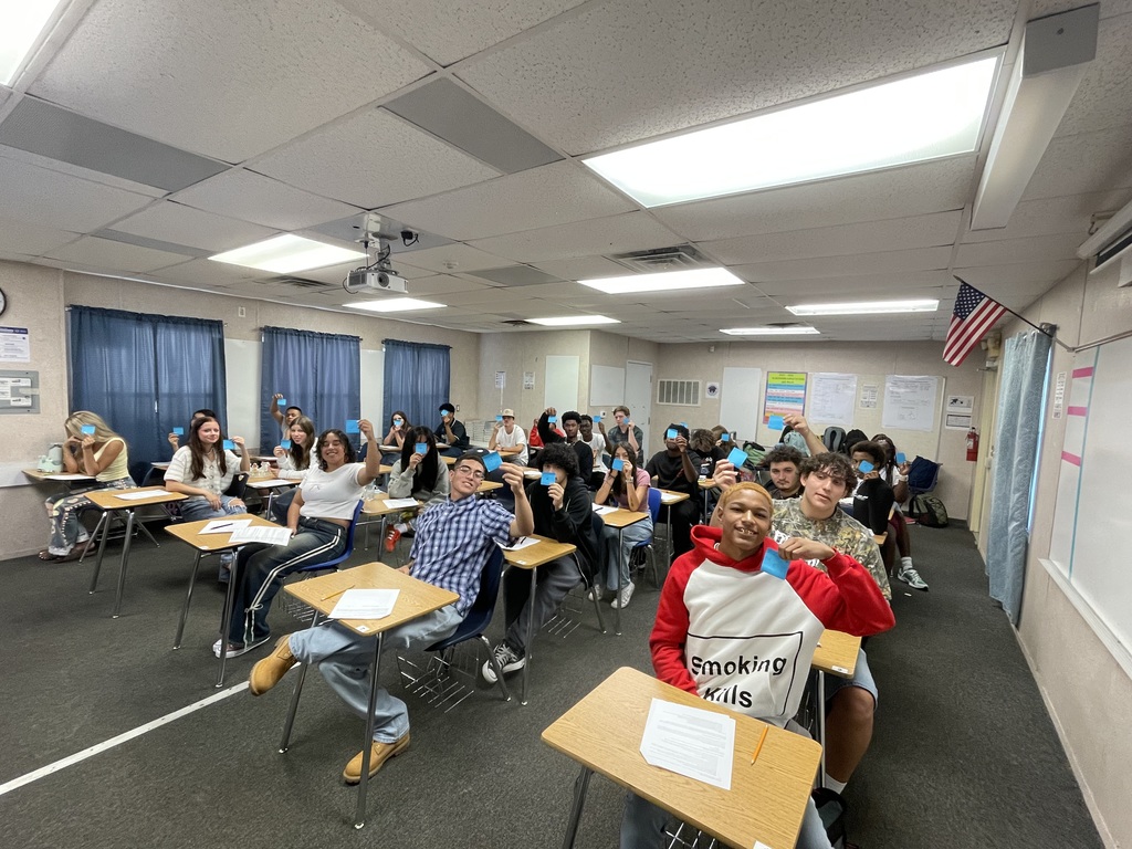 Students in a classroom holding up colorful sticky notes with emojis showing how they feel about the first day of math class.
