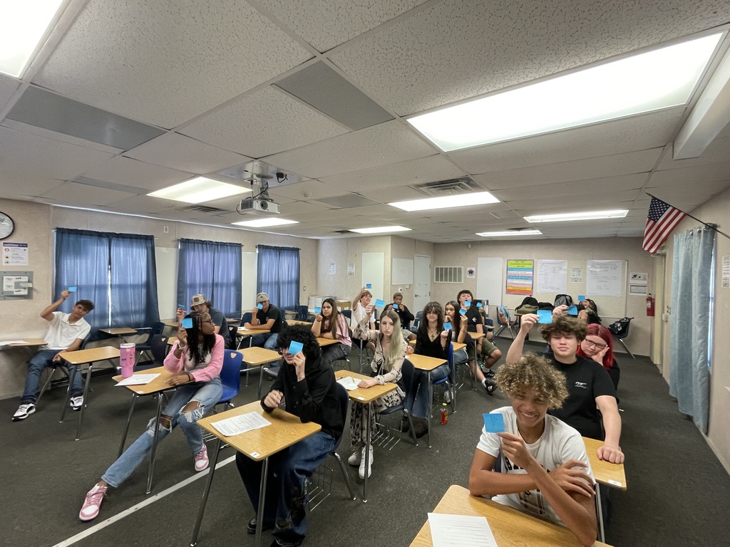Students in a classroom holding up colorful sticky notes with emojis showing how they feel about the first day of math class.