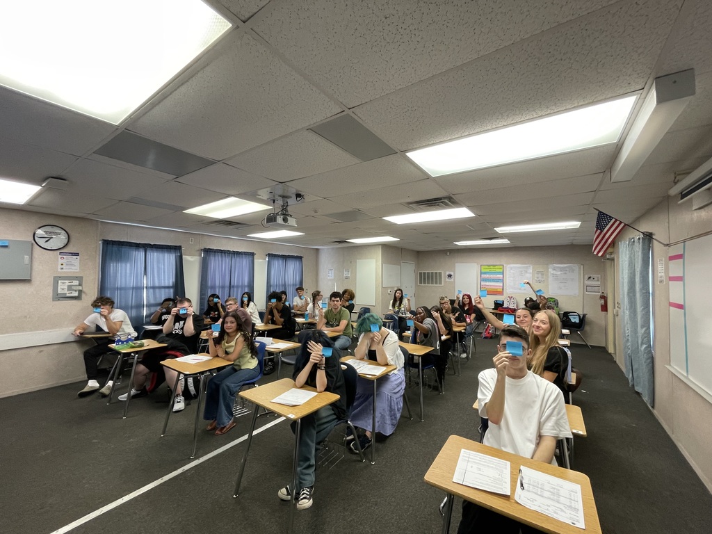 Students in a classroom holding up colorful sticky notes with emojis showing how they feel about the first day of math class.