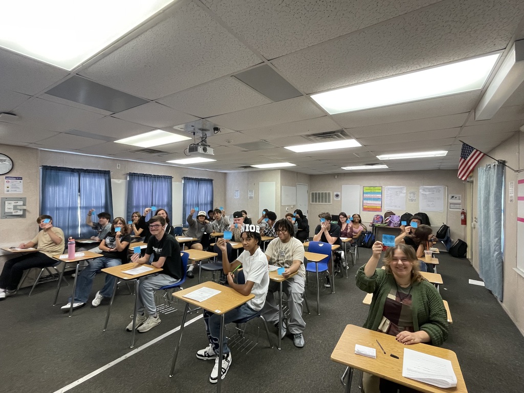 Students in a classroom holding up colorful sticky notes with emojis showing how they feel about the first day of math class.