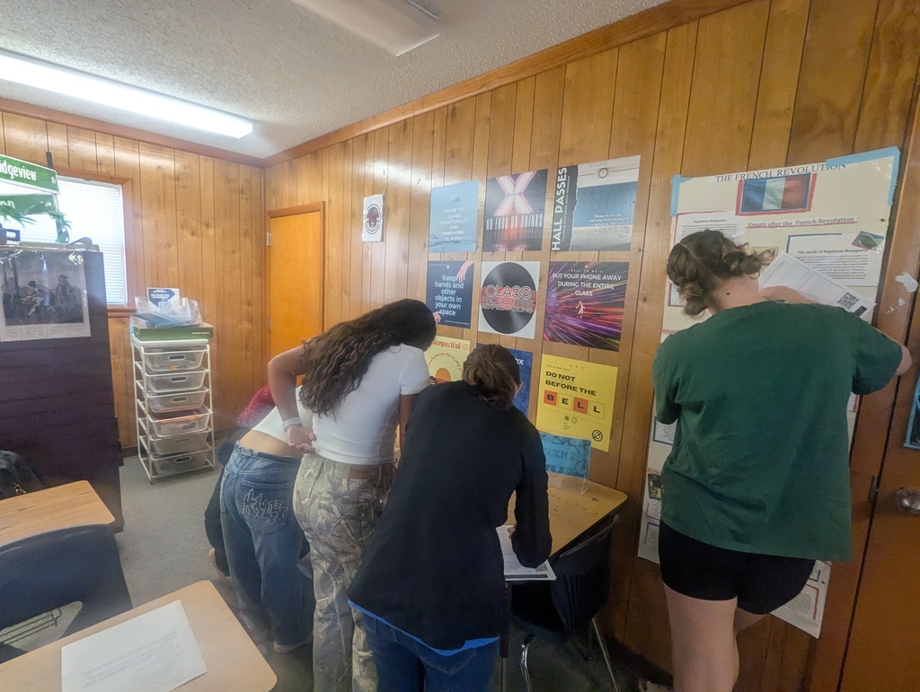 High school students moving between stations in a classroom, reading signs and materials to learn about expectations, procedures, and where to find supplies and textbooks.