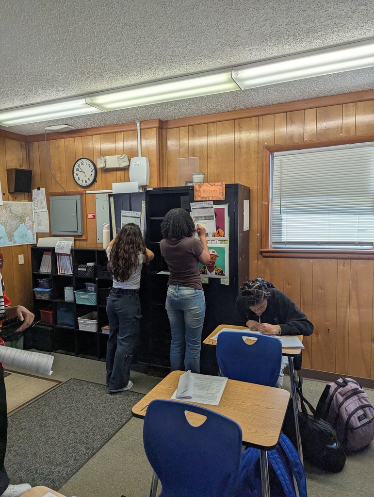 High school students moving between stations in a classroom, reading signs and materials to learn about expectations, procedures, and where to find supplies and textbooks.
