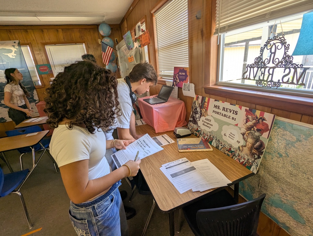 High school students moving between stations in a classroom, reading signs and materials to learn about expectations, procedures, and where to find supplies and textbooks.