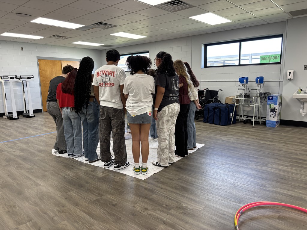 CNA students standing on a large bedsheet, working together to flip it over without letting it touch the floor during a teamwork challenge.