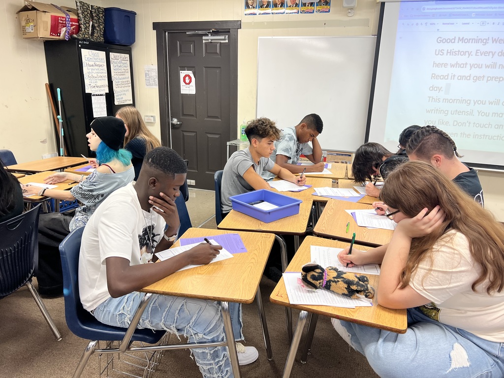 Group of high school students seated in clusters, writing on papers during a classroom activity in US History.