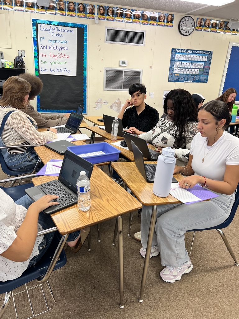 Students working on laptops and completing worksheets during US History class group work.
