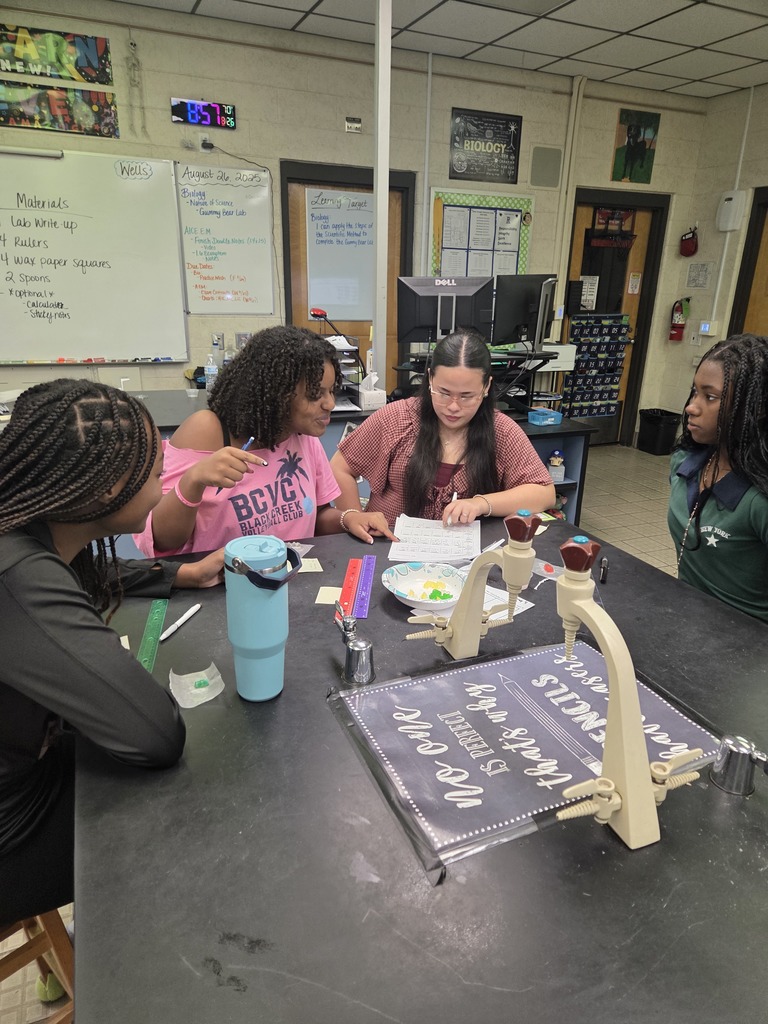 Students in small groups at lab tables measuring gummy bears and recording data in notebooks.