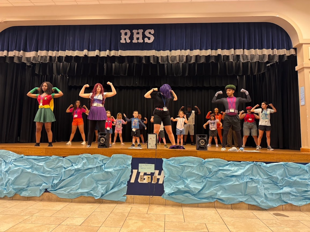 Theatre students on stage dressed as superheroes leading a performance with younger students following their movements.