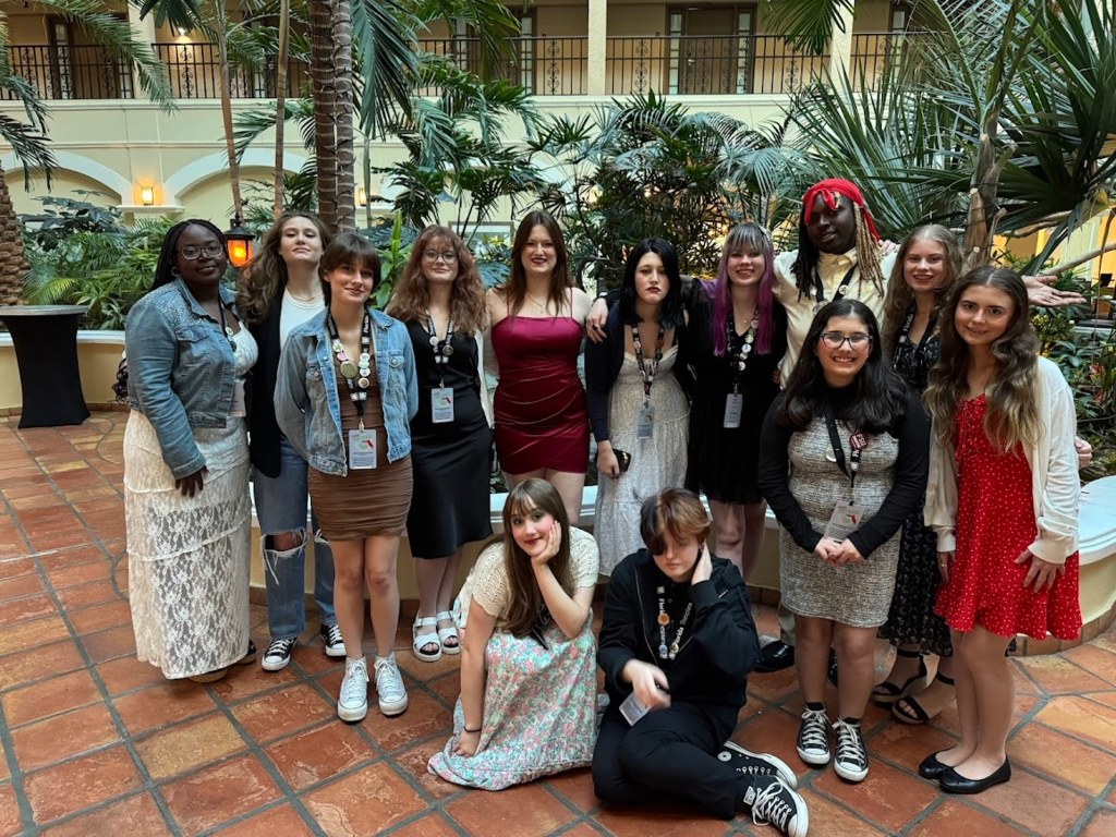 Group of theatre students dressed up and posing together in a hotel atrium during a field trip or performance event.