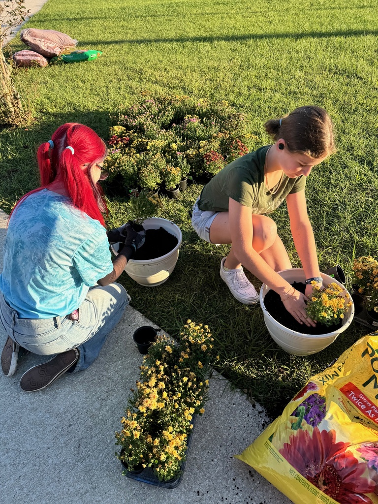 Two students work on transplanting potted plants into the garden area at LAJH.