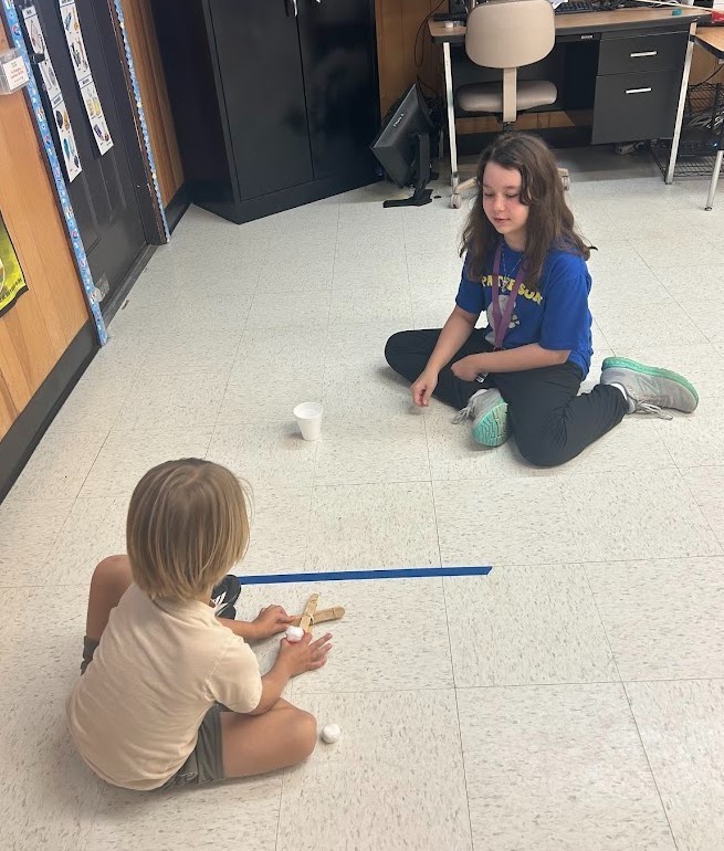6th grade and Kindergarten have both been working on Force and Motion this quarter. Today they paired up in our Science Lab to use catapults, built by 6th graders, to launch cotton balls at targets with our K friends….It was awesome!